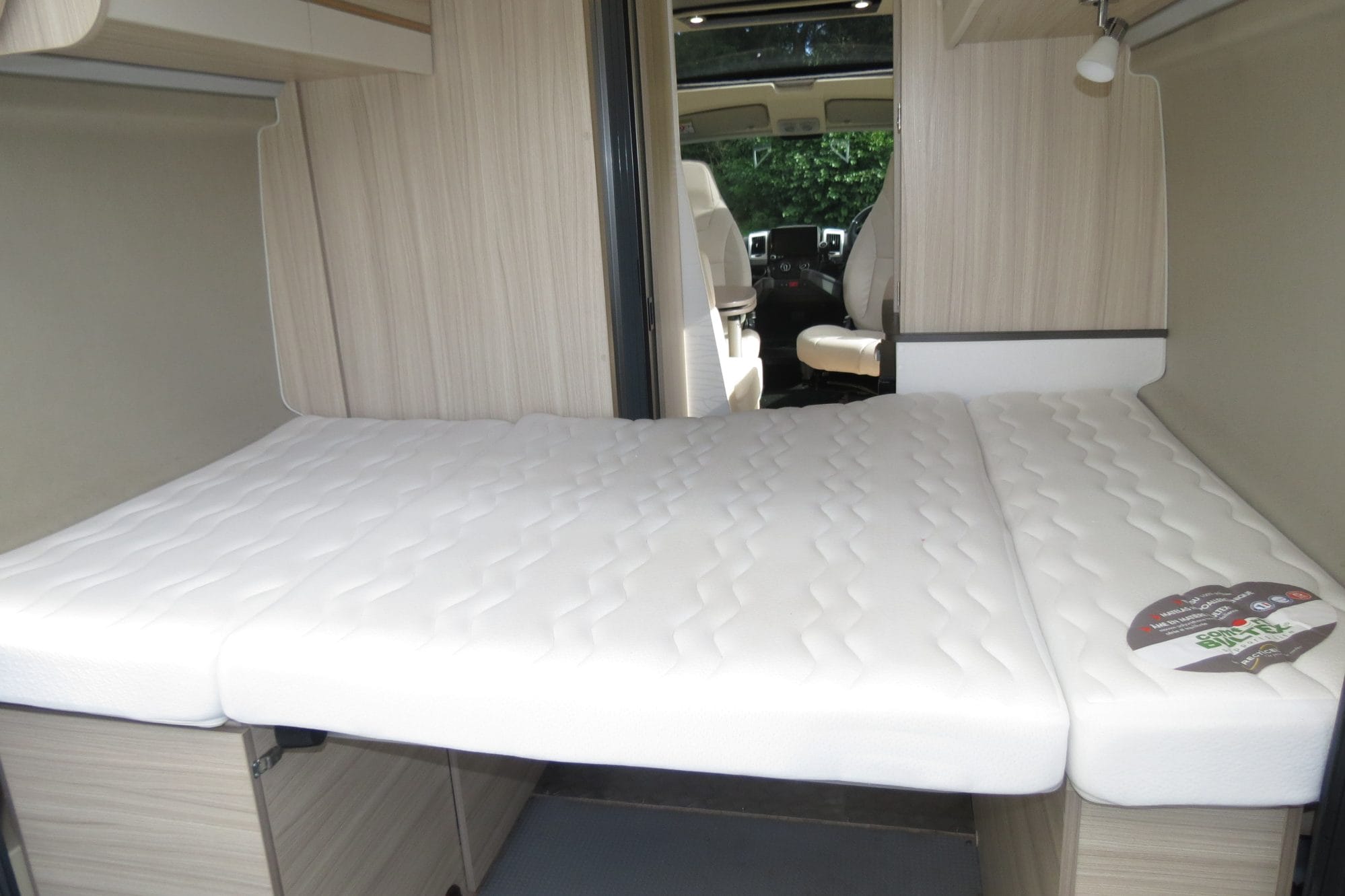 Rear transverse double bed inside Dreamer D43 UP with overhead storage cupboards and reading lights.